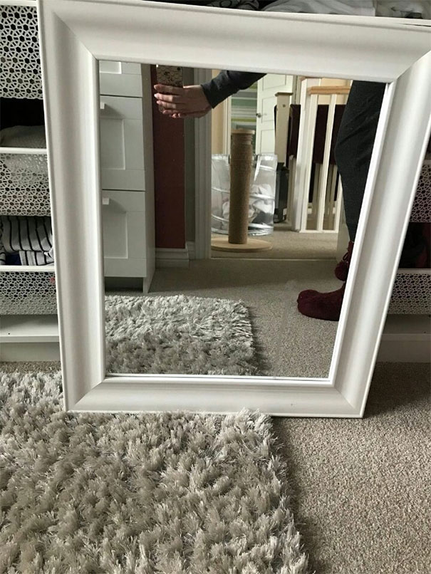 Person holding a white-framed mirror in a carpeted room, showcasing quirky mirror selling attempts.