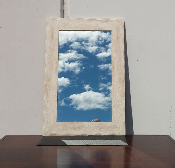 Mirror reflecting a cloudy sky, creating an illusion against a plain wall background.