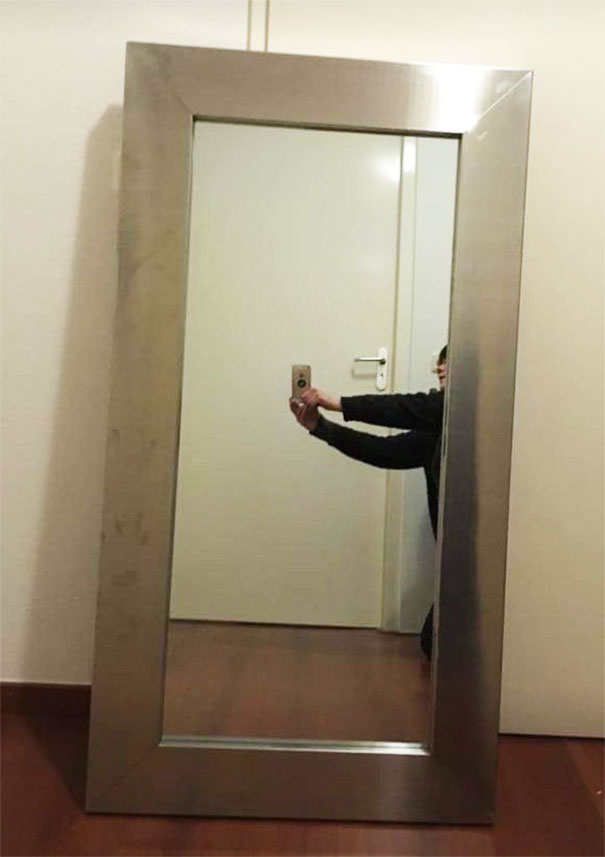 Person taking a photo of a large mirror in a hallway, showcasing creative mirror-selling techniques.