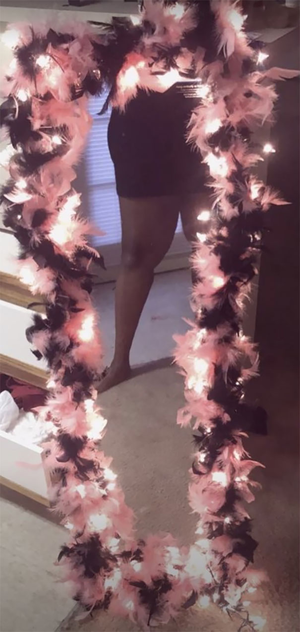 Woman selling a decorated mirror with pink and black feathers, reflecting partially in the room.