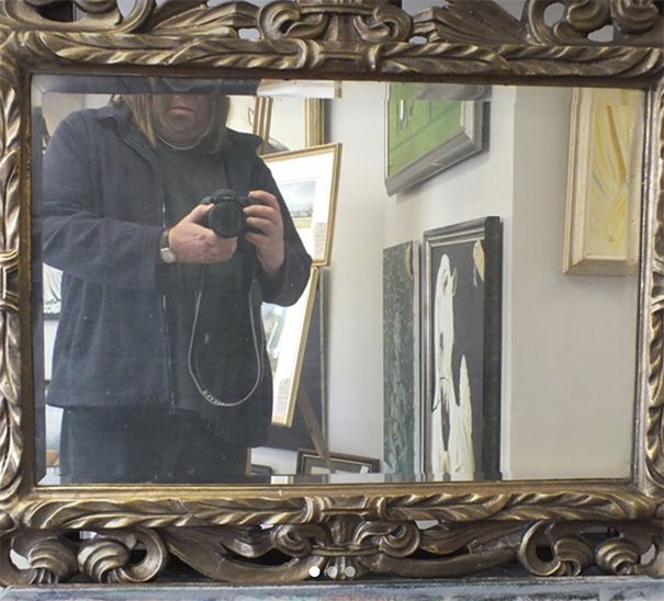 Person taking photo in a mirror, capturing reflection in ornate frame, related to selling mirrors.