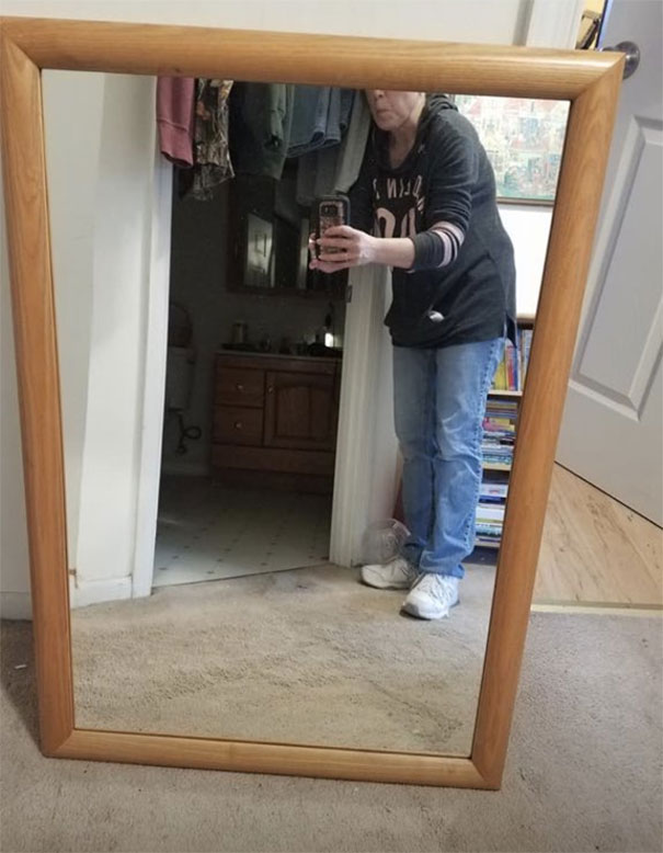 Person trying to sell a mirror, taking a photo of the mirror on a beige carpet with a wooden frame.