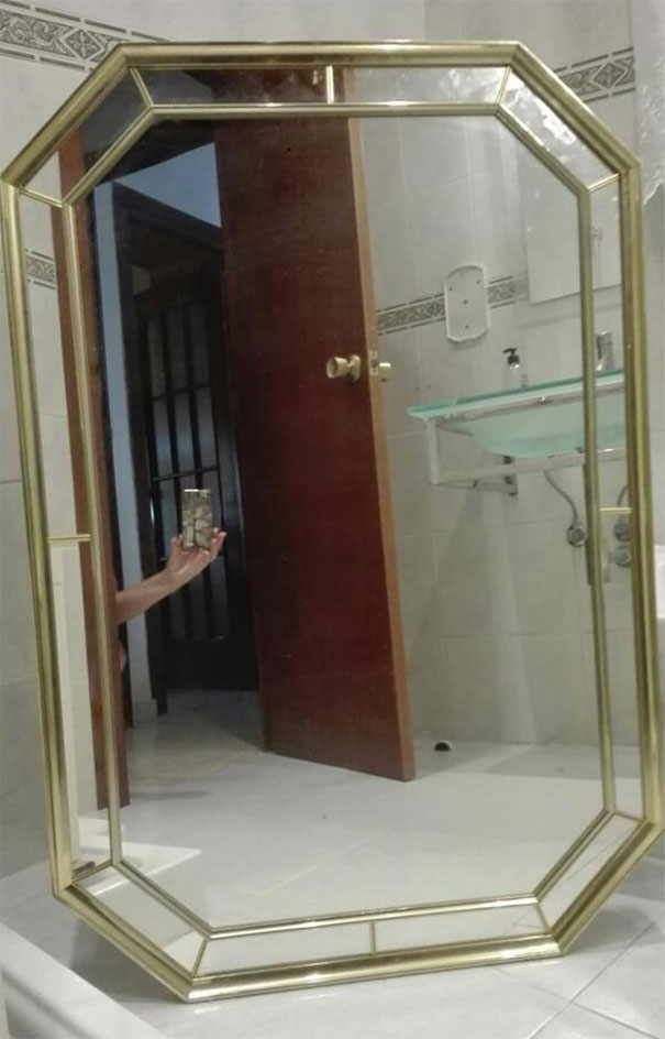 Mirror with gold frame in a bathroom, showcasing a person’s hand holding a phone for a creative sales photo.