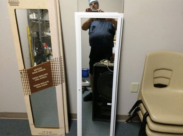 Person taking a photo of a mirror for sale, reflection showing part of the room including chairs and cardboard packaging.