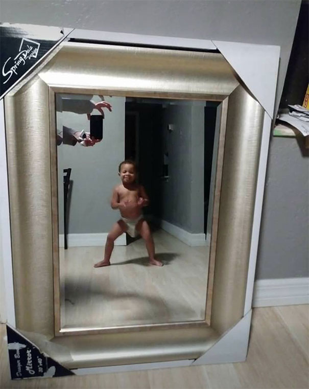 Child reflected in a mirror for sale, posing playfully in a diaper, showcasing mirror's reflection quality.