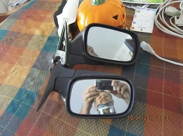 Mirrors for sale with a reflection of a person taking a photo, next to a pumpkin on a plaid tablecloth.