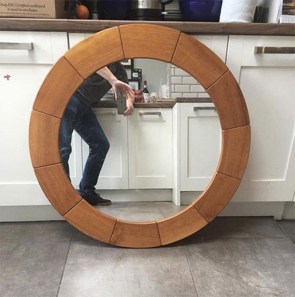 Person's arm visible as they take a photo of a large round mirror in a kitchen setting.
