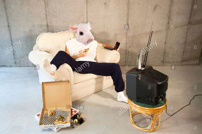 Man with pink pig head in the basement watching TV eating pizza and drinking beer