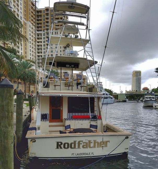 Clever named tall fishing boat docked near houses 