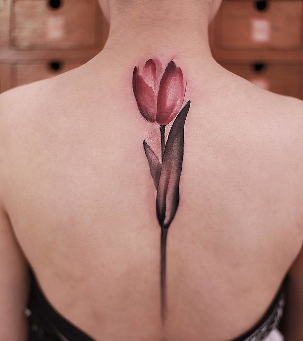 Elegant spine tattoo of a red tulip on woman's back.