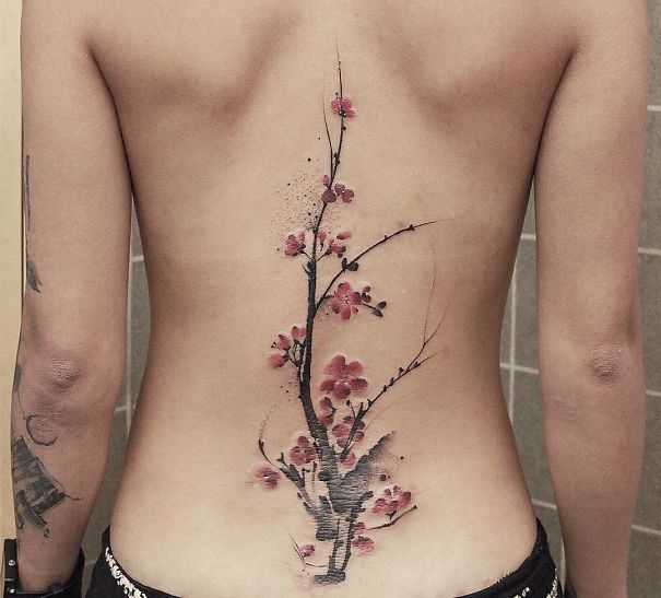 Cherry blossom spine tattoo on a person's back, featuring delicate branches and pink flowers.