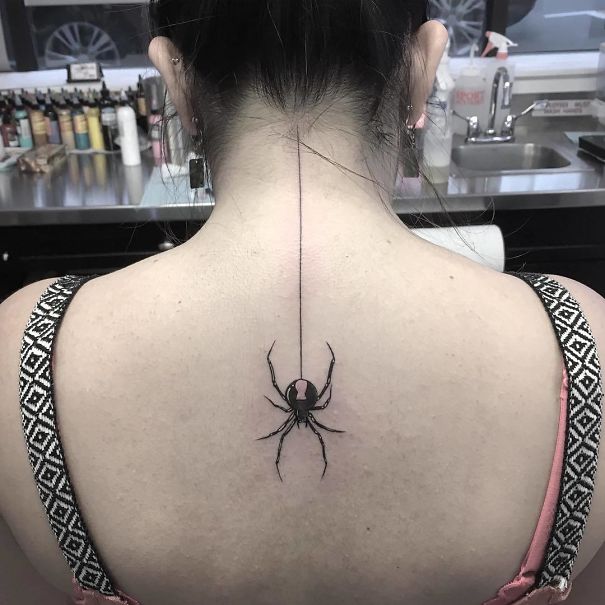 Spider tattoo design on the spine of a woman's back in a tattoo studio.
