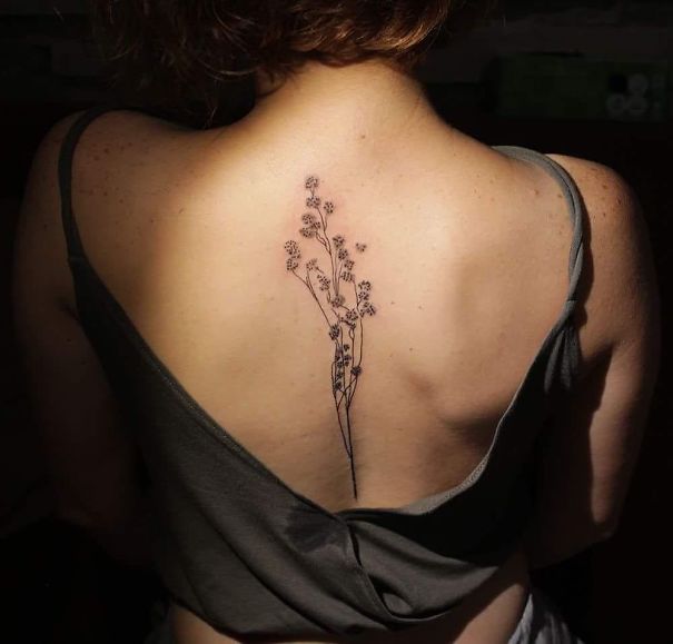 Minimalist floral spine tattoo on woman's back with open-back top.
