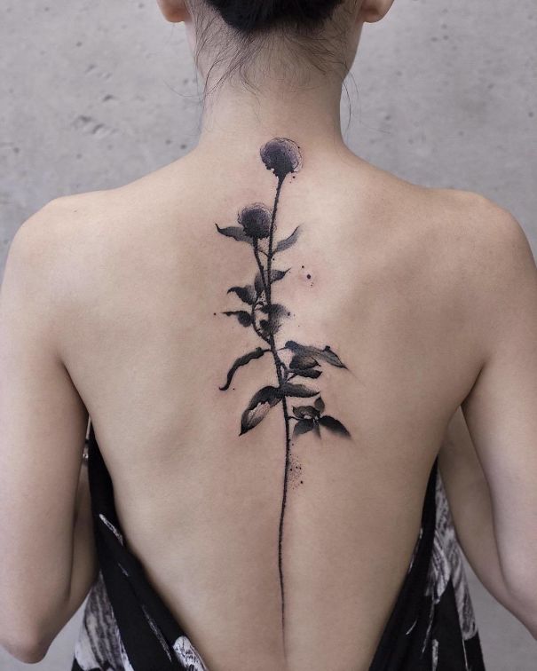 Elegant black ink flower spine tattoo on a woman's upper back.