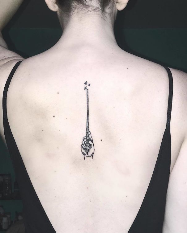 Minimalist spine tattoo featuring a detailed hand and stars design on a woman's back.