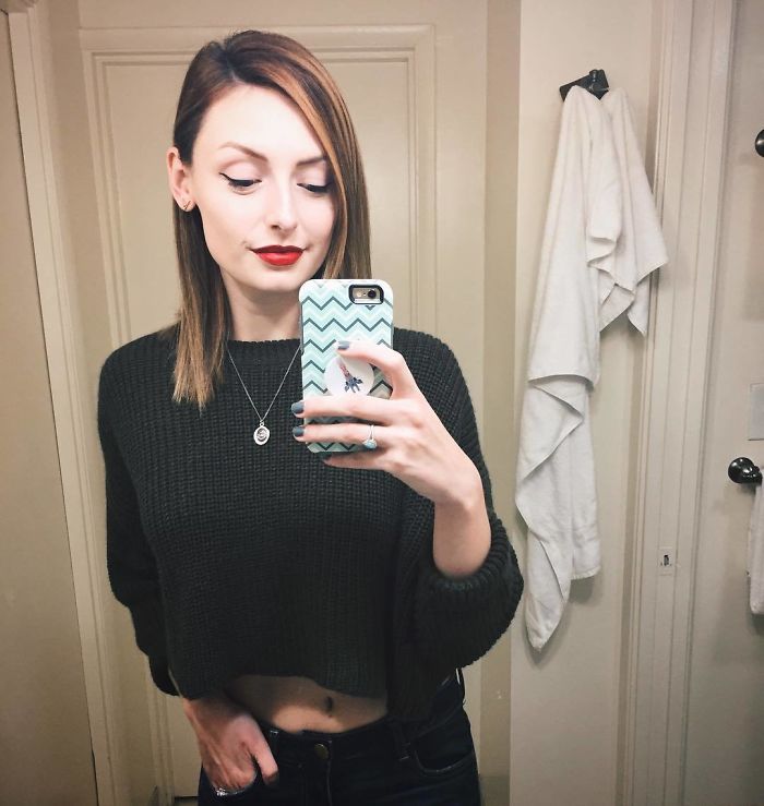 Woman taking a mirror selfie, showcasing intact eyeliner and red lipstick, wearing a dark sweater. Woman taking a mirror selfie, showcasing intact eyeliner and red lipstick, wearing a dark sweater.