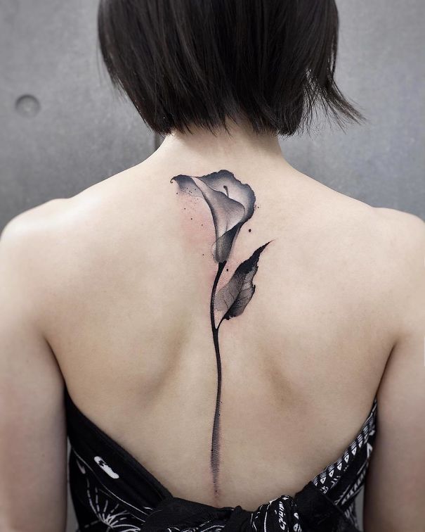 Floral spine tattoo in black and gray ink on woman's back.