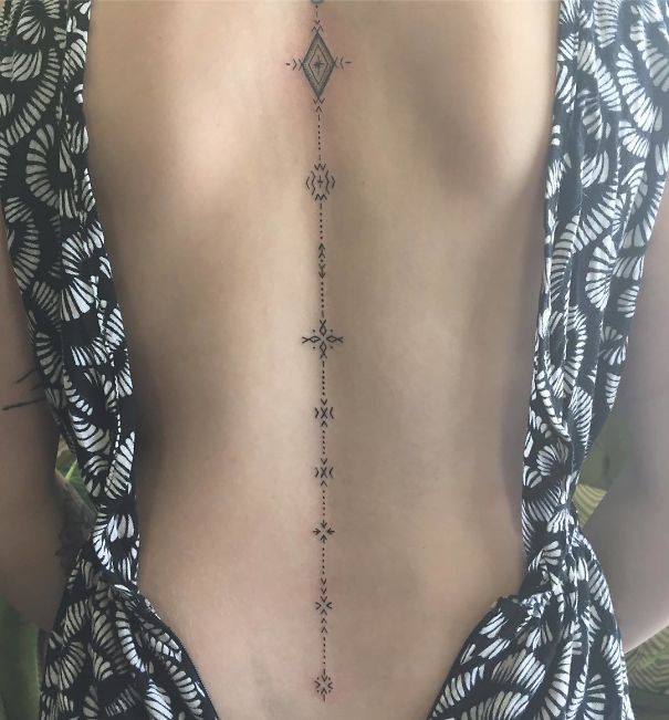 Intricate geometric spine tattoo in black ink on a woman's back, framed by a patterned blouse.
