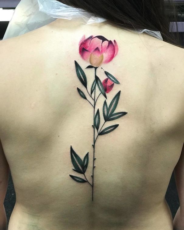 Female back with a floral spine tattoo featuring a pink flower and green leaves.