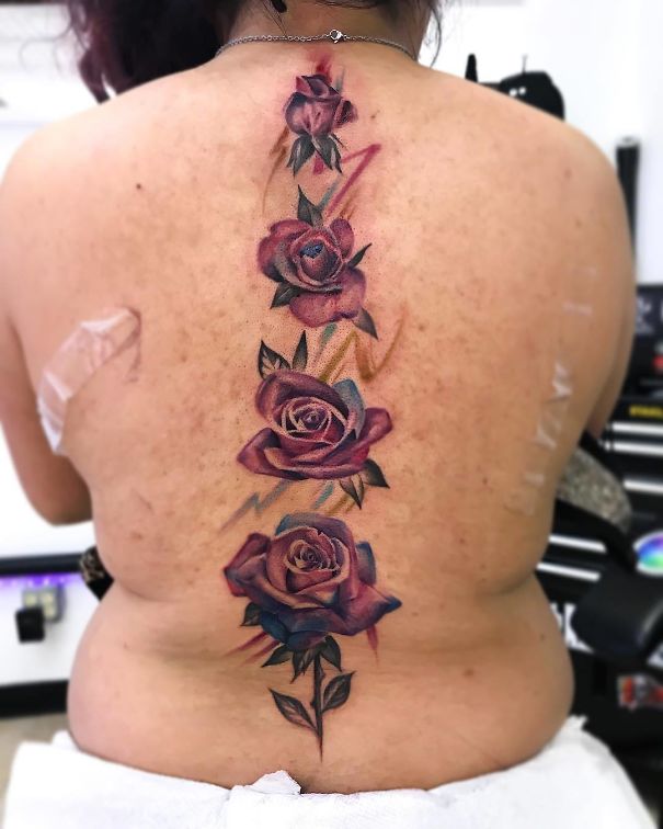 Colorful rose spine tattoo on a woman's back, showcasing intricate details and vibrant hues.