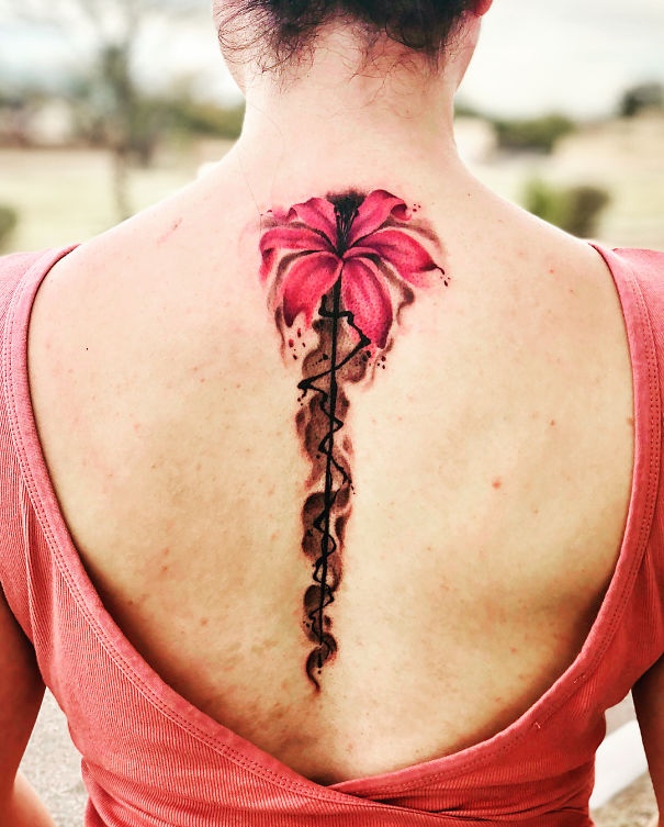 Pink flower spine tattoo design on a woman's back wearing a sleeveless top.