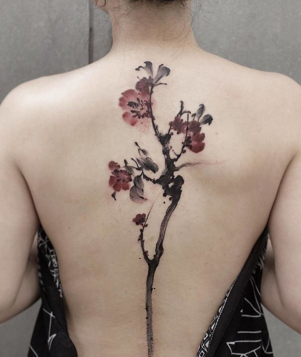 Elegant cherry blossom spine tattoo with black and red ink detailing.