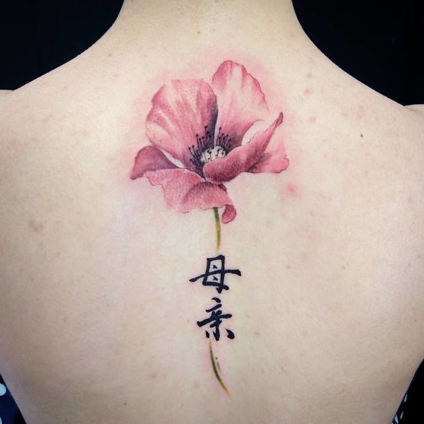 Delicate spine tattoo with a pink flower and Chinese characters, showcasing one of the best spine tattoo ideas.