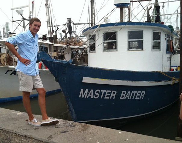 Man standing next to a funny named white and blue boat 