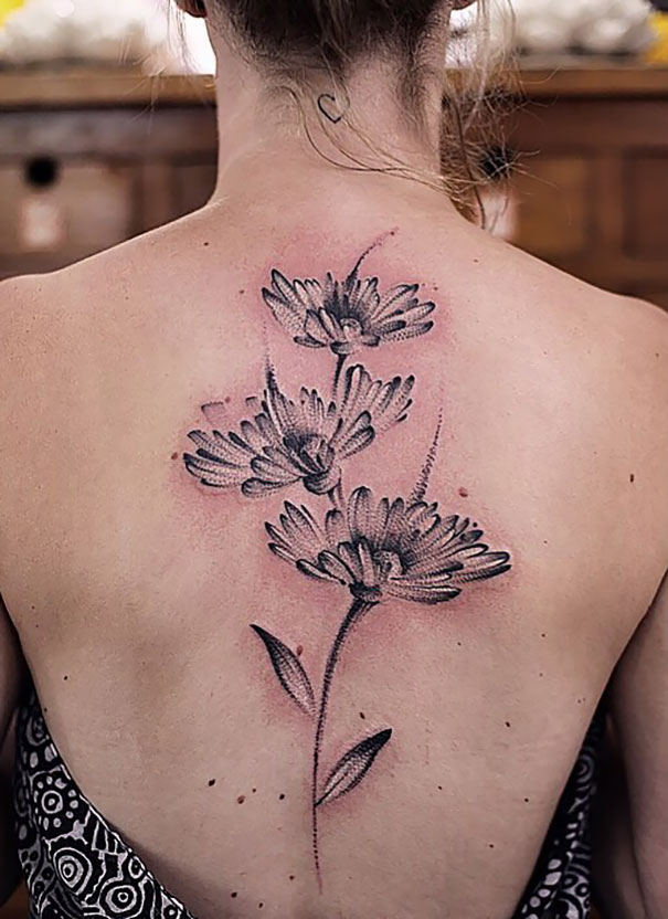 Floral spine tattoo design featuring bold, black flowers on a woman's back.