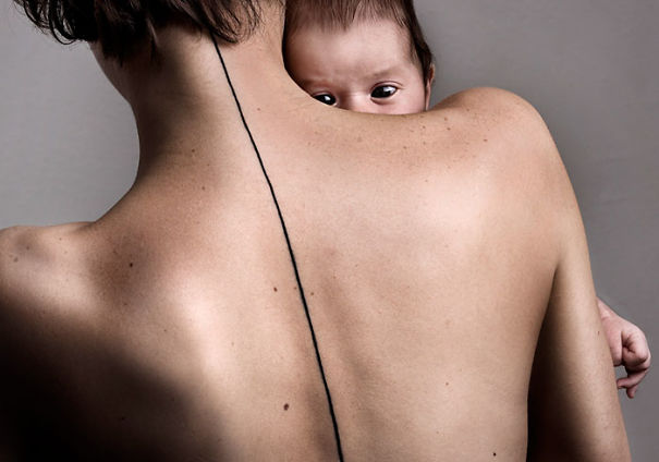 Minimalist spine tattoo on a person's back while holding a baby.