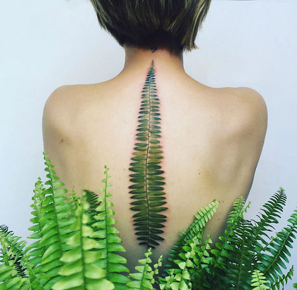 Fern-inspired spine tattoo, detailed and elegant, surrounded by lush green plants.