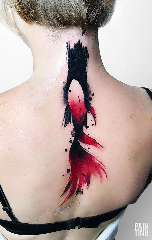 Abstract red and black spine tattoo on a woman's upper back, resembling a fish.