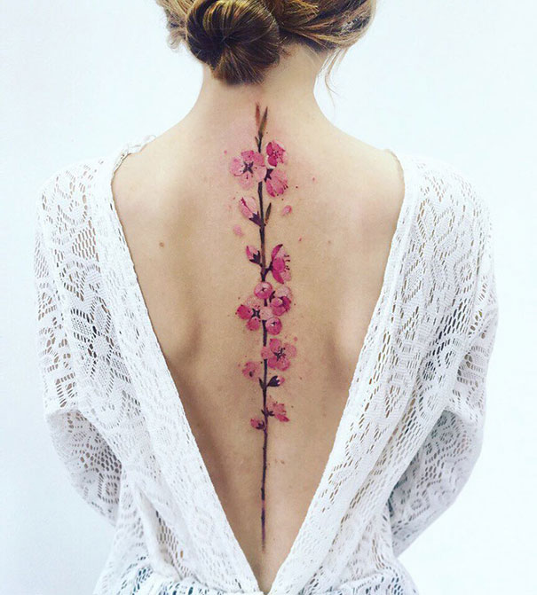 Pink cherry blossom spine tattoo on woman's back, wearing a lace dress.