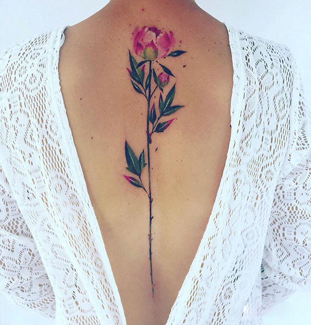 Floral spine tattoo on a woman's back in a white lace top.