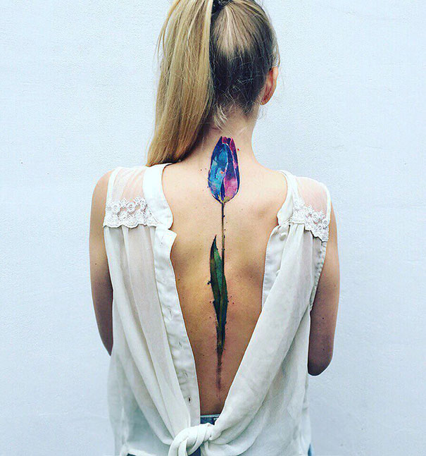 Woman with a colorful tulip spine tattoo, wearing a backless blouse, showcasing unique body art design.