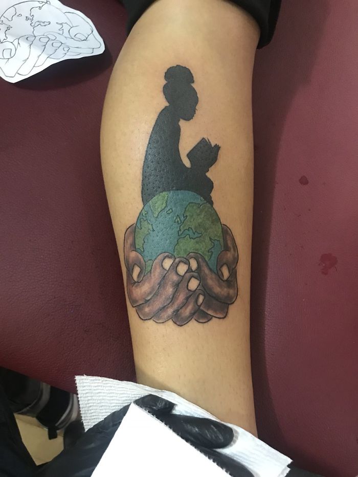 Tattoo on arm of hands holding Earth, silhouette reading book. Artist skillfully depicted client's idea. Tattoo on arm of hands holding Earth, silhouette reading book. Artist skillfully depicted client's idea.