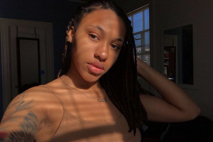 Sierra Alexis with a tattoo, showcasing artistry; sunlight casting shadows indoors.