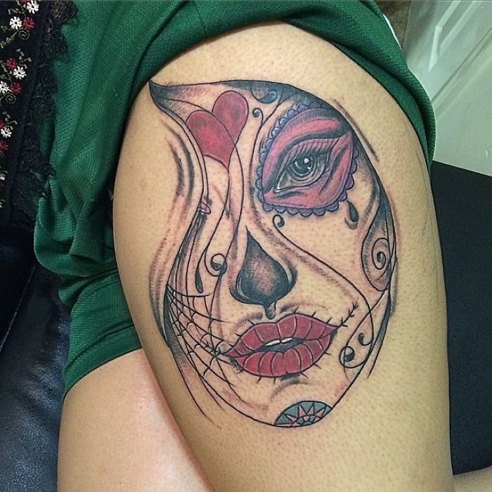 Tattoo artist's skill transforms a whimsical sketch into a vibrant mask-face tattoo on a person's arm.