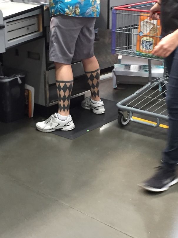 Man with diamond-patterned leg tattoos resembling socks, wearing sneakers and shorts in a store setting.