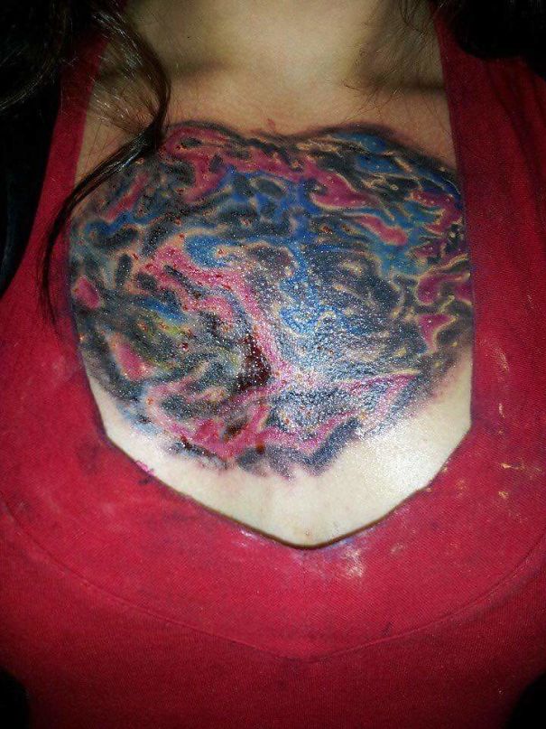 Close-up of a colorful tattoo mishap on a person's chest, resembling abstract art, surrounded by red fabric.