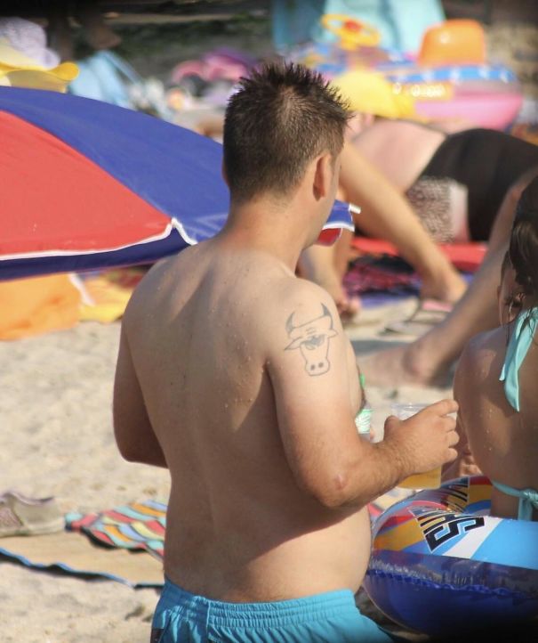 Man with a comical bull tattoo on shoulder at the beach, showcasing a tattoo fail.