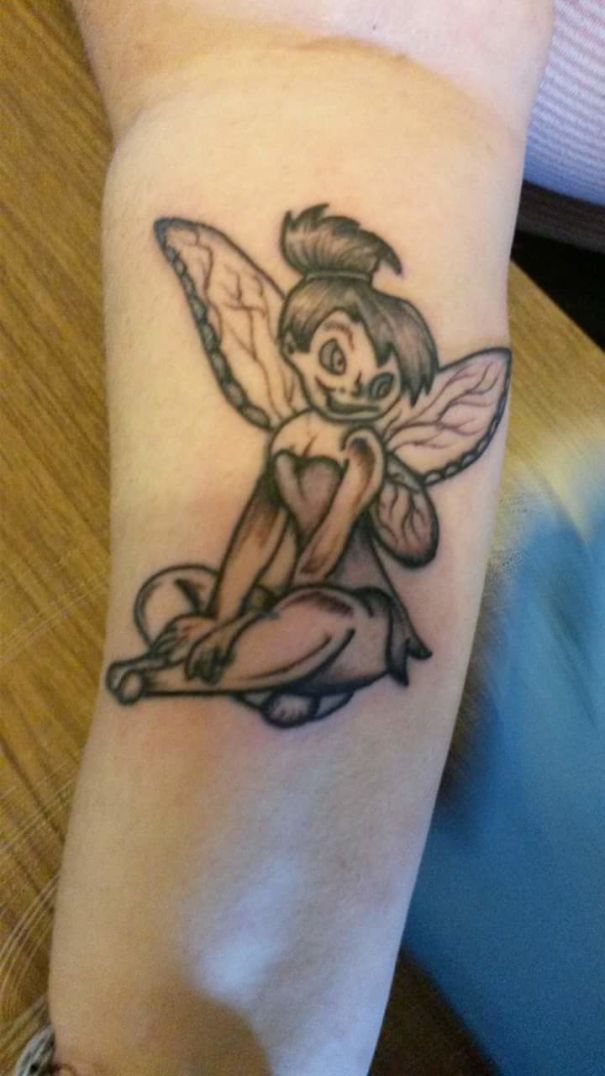 Fairy tattoo fail with awkward expression and uneven lines on forearm.