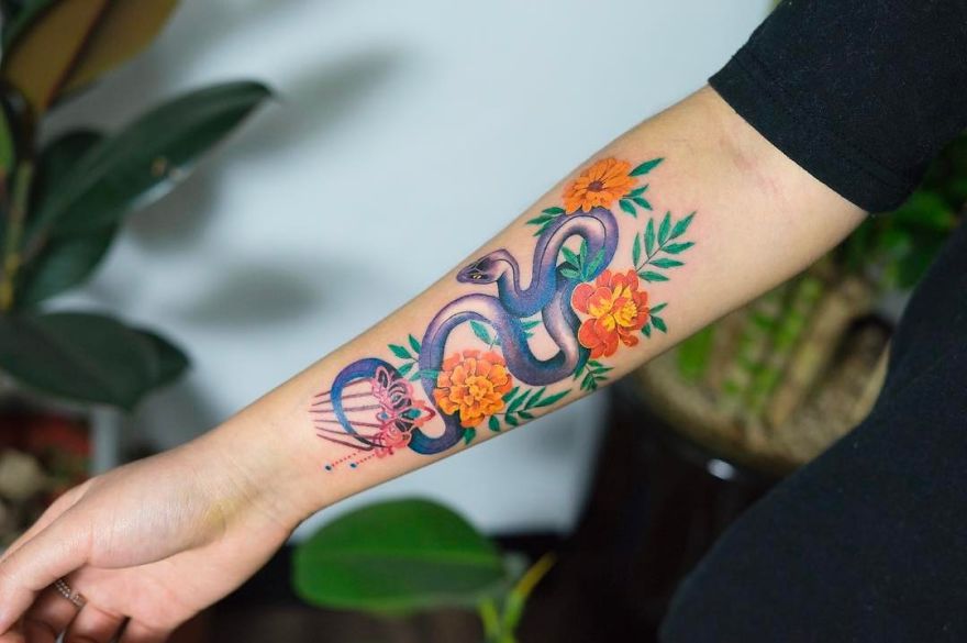 Korean artist's snake tattoo with colorful flowers on forearm.