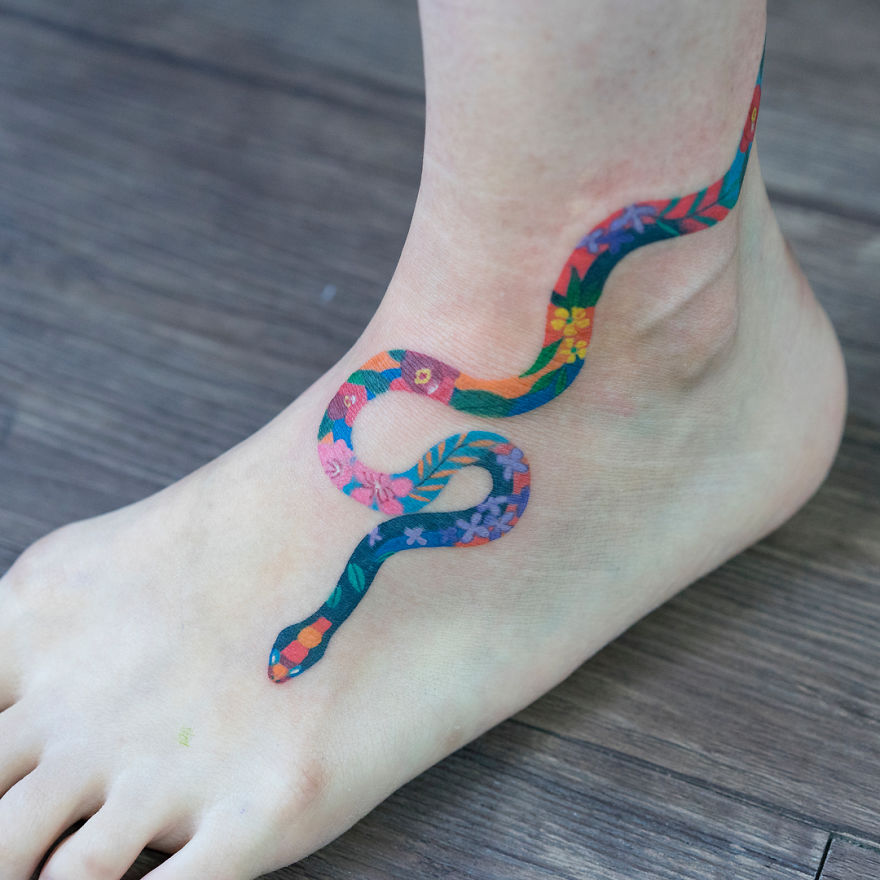 Colorful snake tattoo on ankle by Korean artist, featuring floral patterns and intricate details.