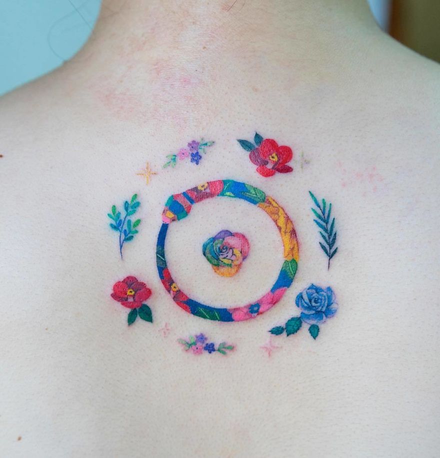 Colorful snake tattoo by Korean artist on back, encircled by flowers and leaves.