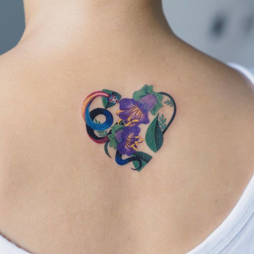 Colorful snake tattoo on a person's shoulder, designed by a Korean artist, incorporating flowers and leaves.