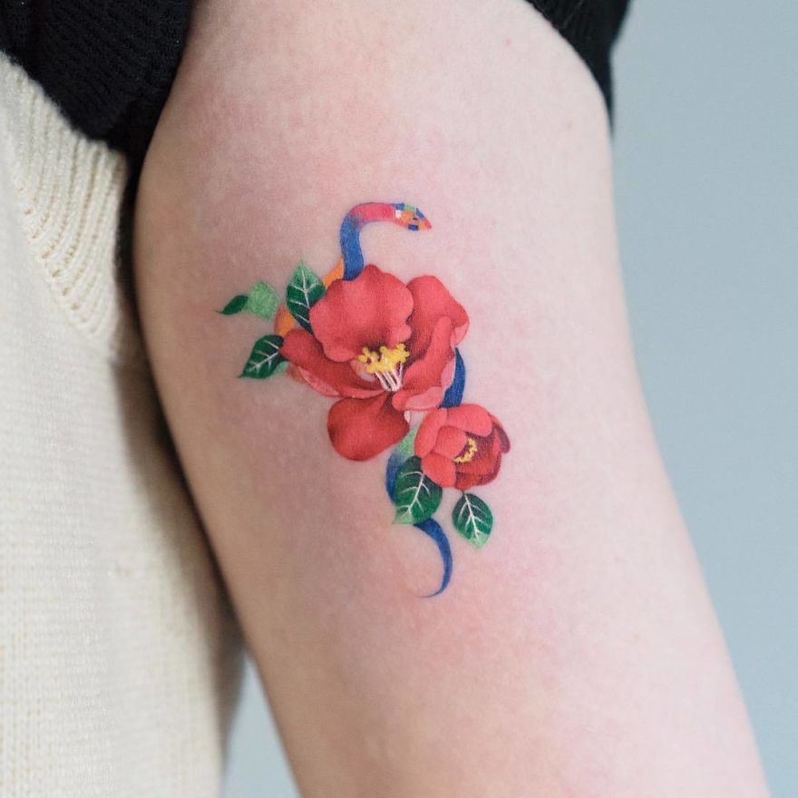 Korean artist designs unique snake tattoo intertwined with vibrant flowers on an arm.