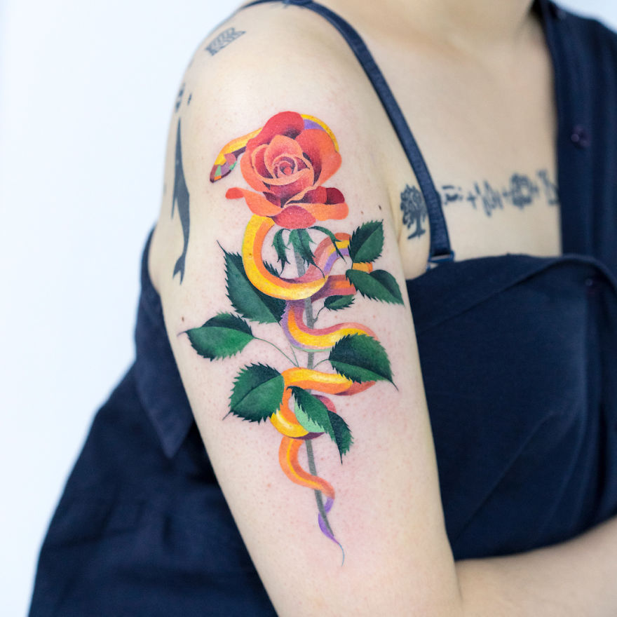 Tattoo of a vibrant snake entwined with a red rose on a person's upper arm, created by a Korean artist.