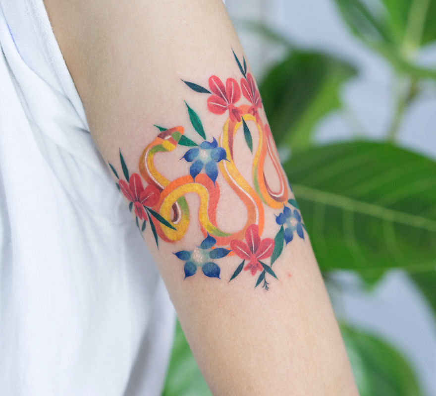 Korean artist's vibrant snake tattoo surrounded by colorful flowers on an arm.