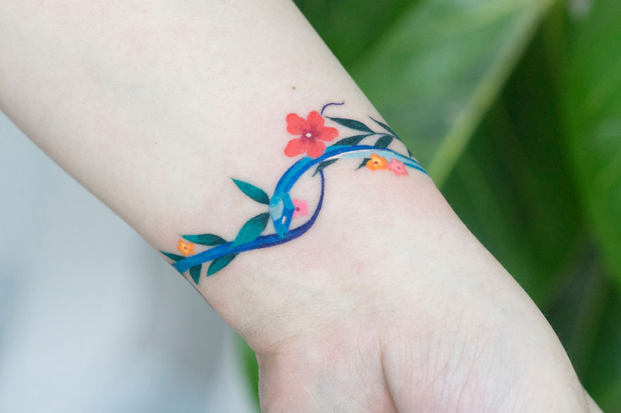 Colorful snake tattoo by Korean artist with floral design on wrist.